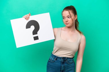 Young caucasian woman isolated on green background holding a placard with question mark symbol