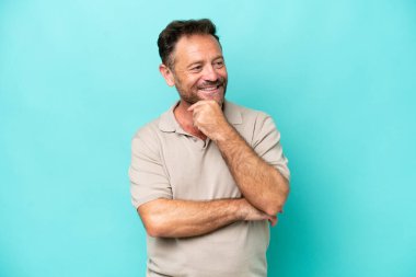 Mavi arka planda soyutlanmış orta yaşlı beyaz bir adam yana bakıyor ve gülümsüyor.