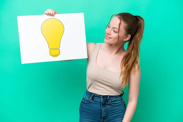 Young Caucasian Woman Isolated Green Background Holding Placard Bulb Icon — Foto Stock