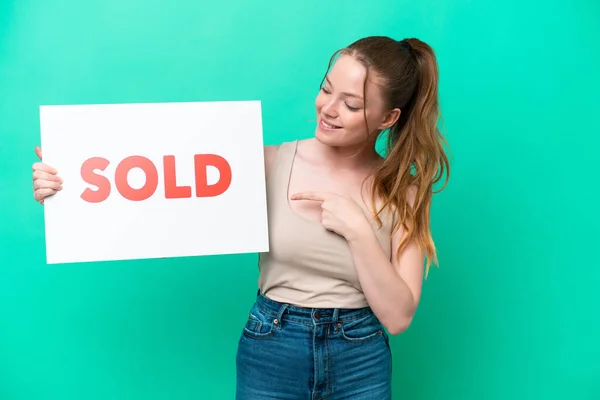 Young Caucasian Woman Isolated Green Background Holding Placard Text Sold —  Fotos de Stock