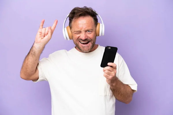 Middelbare Leeftijd Kaukasische Man Geïsoleerd Paarse Achtergrond Luisteren Muziek Met — Stockfoto