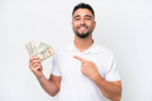 Young Arab man taking a lot of money isolated on white background pointing to the side to present a product