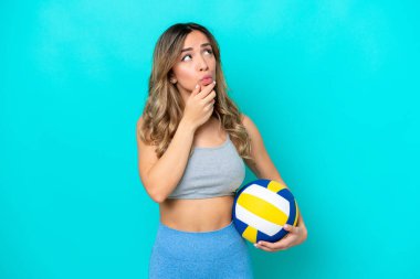 Genç beyaz kadın voleybol oynuyor. Mavi arka planda izole edilmiş. Şüpheleri var.