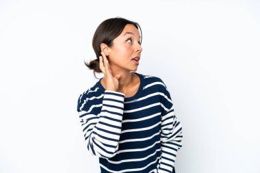 Young hispanic woman isolated on white background listening to something by putting hand on the ear