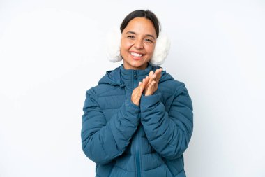 Young hispanic woman wearing a winter earmuffs isolated on white background applauding after presentation in a conference