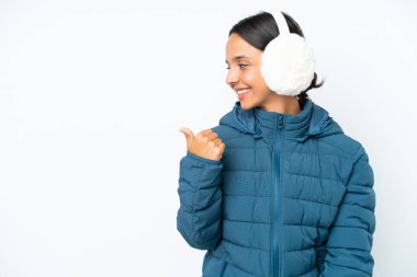 Young hispanic woman wearing a winter earmuffs isolated on white background pointing to the side to present a product