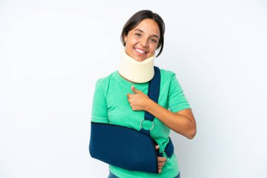 Young hispanic woman wearing a neck brace and sling isolated on white background giving a thumbs up gesture