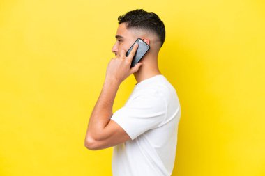 Young Arab handsome man isolated on yellow background keeping a conversation with the mobile phone with someone