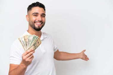 Young Arab man taking a lot of money isolated on white background extending hands to the side for inviting to come