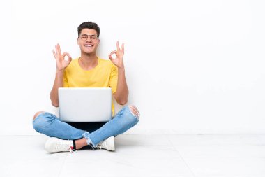 Young man sitting on the floor isolated on white background in zen pose