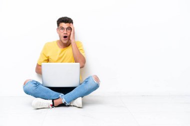 Young man sitting on the floor isolated on white background with surprise and shocked facial expression