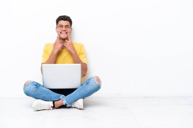 Young man sitting on the floor isolated on white background smiling with a happy and pleasant expression
