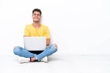 Young man sitting on the floor isolated on white background with arms crossed and looking forward