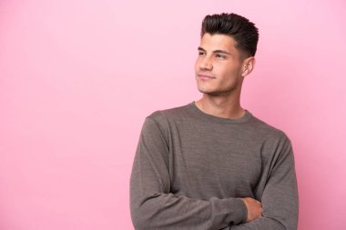Pembe arka planda izole edilmiş genç beyaz adam yan tarafa bakıyor.