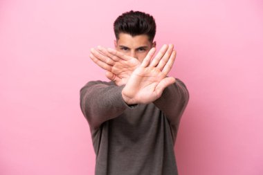 Pembe arka planda izole edilmiş genç beyaz adam bir hareketi durdurmak için eliyle jest yapıyor.