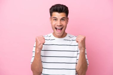 Pembe arka planda izole edilmiş genç beyaz adam galibiyeti kutluyor.