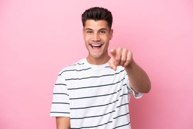 Pembe arka planda izole edilmiş genç beyaz adam şaşırmış ve ön tarafı işaret ediyor.