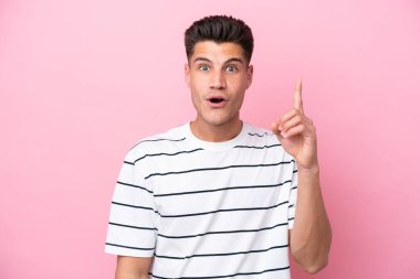 Pembe arka planda izole edilmiş genç beyaz adam çözümü bulmak için parmağını kaldırıyor.