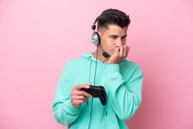 Pembe arka planda izole edilmiş bir bilgisayar oyunu kontrolörüyle oynayan yakışıklı beyaz bir adam.
