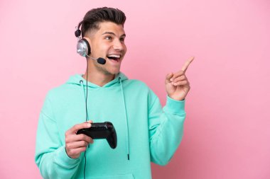 Pembe arka planda izole edilmiş bir bilgisayar oyunu kontrolörüyle oynayan yakışıklı beyaz adam çözümü bulmak için parmağını kaldırıyor.