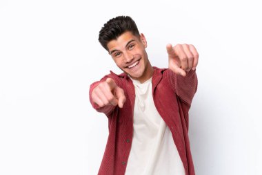 Beyaz arka planda izole edilmiş genç beyaz adam mutlu bir ifadeyle ön tarafı işaret ediyor.