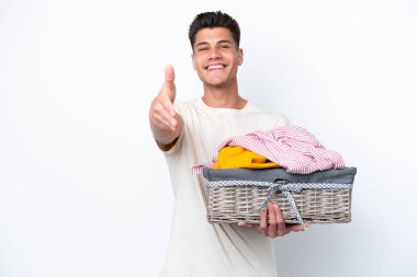 Young caucasian man holding laundry basket isolated on white background shaking hands for closing a good deal