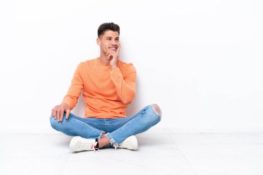 Genç bir adam beyaz arka planda izole bir şekilde yerde oturuyor.