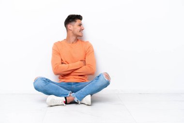 Yerde oturan genç adam, beyaz arka planda yan pozisyonda izole edilmiş.