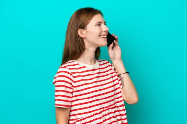 Mavi arka planda izole edilmiş genç bir İngiliz kadın cep telefonuyla sohbet ediyor.
