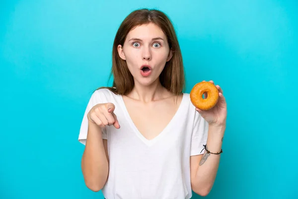 Young English Woman Holding Donut Isolated Blue Background Surprised Pointing — стоковое фото
