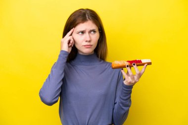 Sarı arka planda saşimi tutan genç İngiliz kadının şüpheleri ve düşünceleri var.