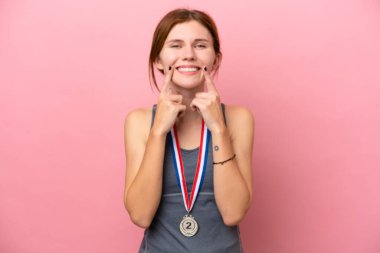 Young English woman with medals isolated on pink background smiling with a happy and pleasant expression