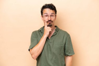 Young caucasian man isolated on beige background and thinking