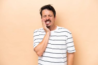 Young caucasian man isolated on beige background with toothache