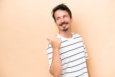 Beyazların arka planında izole edilmiş genç beyaz bir adam bir ürün sunmak için kenarı işaret ediyor.