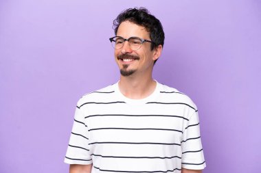 Young caucasian man isolated on purple background With glasses with happy expression
