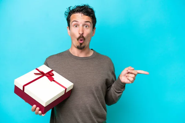Young Man Holding Gift Surprised Pointing Side — Stockfoto