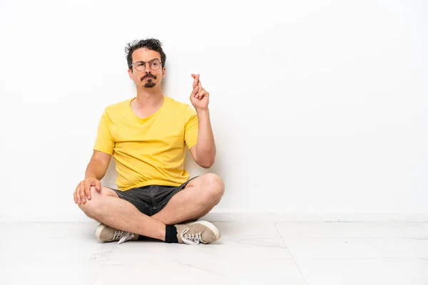 Young Caucasian Man Sitting Floor Isolated White Background Fingers Crossing — Foto de Stock