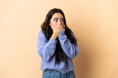 İzole edilmiş arka planda genç beyaz kadın ağzını kapatıyor ve yan tarafa bakıyor.