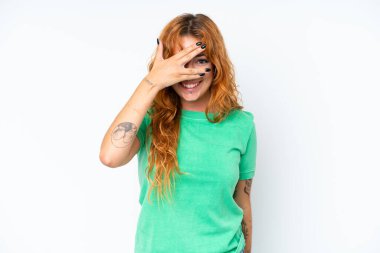 Beyaz arka planda soyutlanmış beyaz tenli genç bir kadın elleriyle gözlerini kapatıyor ve gülümsüyor.