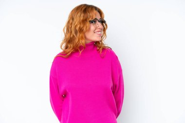 Beyaz arka planda izole edilmiş genç beyaz kadın yan bakıyor ve gülümsüyor.