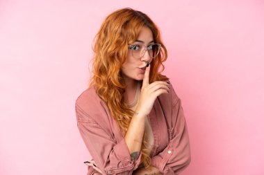 Pembe arka planda gözlüklü ve sessiz hareketler yapan beyaz bir kadın.