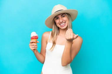 Mavi arka planda izole edilmiş kornet dondurması olan mayo giymiş genç beyaz bir kadın bizi davet ediyor. Gelmene sevindim.