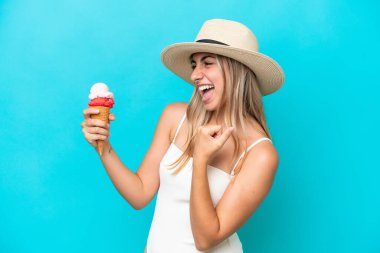 Young caucasian woman in swimsuit with a cornet ice cream isolated on blue background celebrating a victory