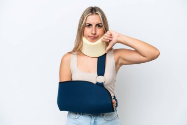 Woman with broken arm and wearing a sling isolated on white background showing thumb down with negative expression