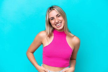 Mavi arka planda izole edilmiş genç beyaz kadın gülüyor.