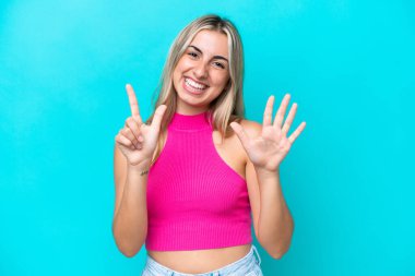 Mavi arka planda izole edilmiş beyaz kadın yediyi parmaklarıyla sayıyor.