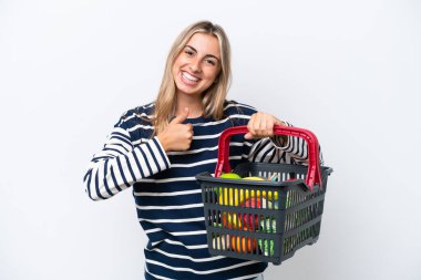 Beyaz arka planda izole edilmiş, elinde yiyecek dolu bir sepet tutan beyaz bir kadın baş parmak işareti yapıyor.