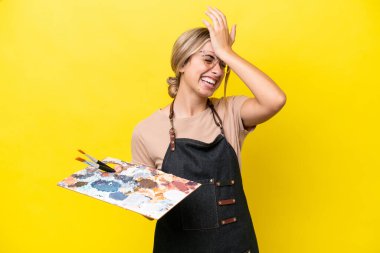 Young artist caucasian woman holding a palette isolated  on yellow background has realized something and intending the solution