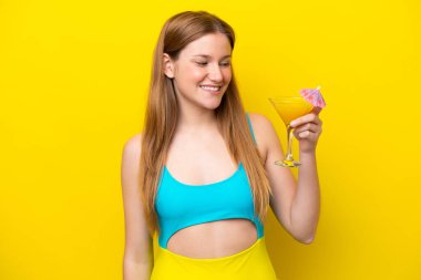 Sarı arka planda neşeli bir ifadeyle izole edilmiş kokteyl tutan beyaz bir kadın.